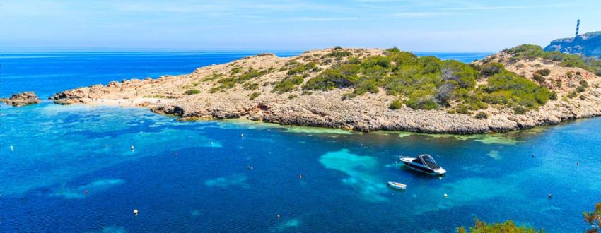 De groene kust met uitzicht op het water en bootjes in de baai van Cala Portinatx op Ibiza